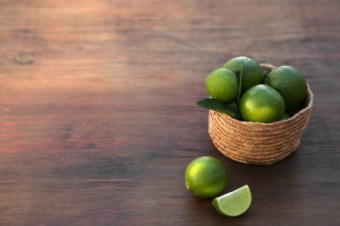 Fresh ripe limes and wicker basket on wooden table. Space for text