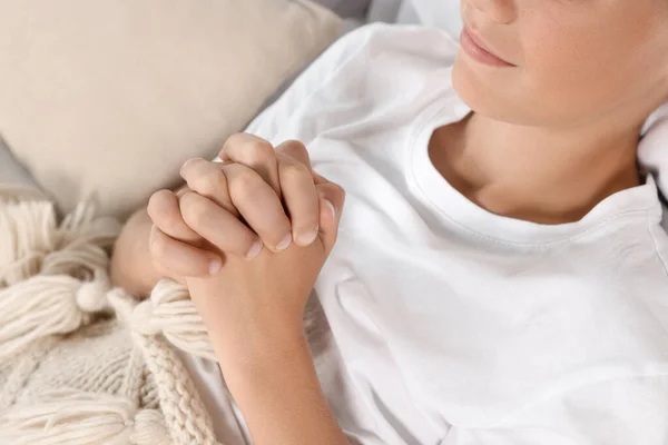 Boy with clasped hands praying in bed, closeup