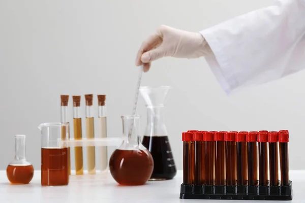 Scientist mixing brown liquid in round bottom flask at table, focus on test tubes