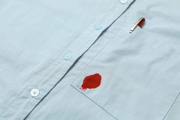 Shirt with stain of red ink and pen in pocket, closeup
