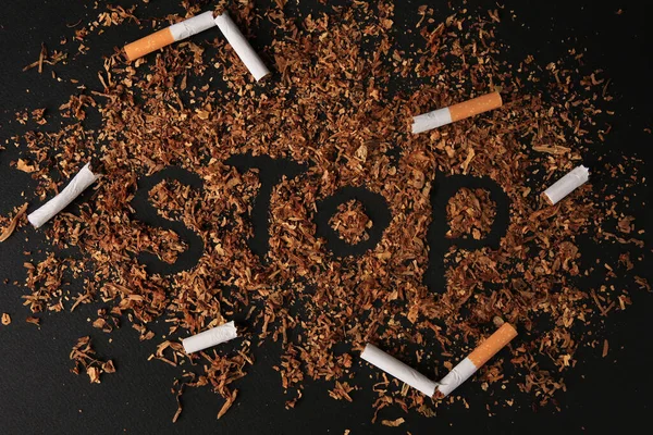 Word Stop made of dry tobacco and broken cigarettes on dark grey background, flat lay. Quitting smoking concept