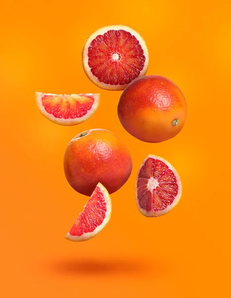 Many tasty Sicilian oranges falling on bright orange background