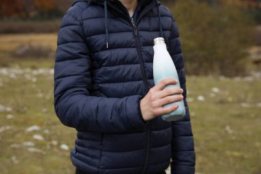 Boy holding thermo bottle with drink in mountains, closeup