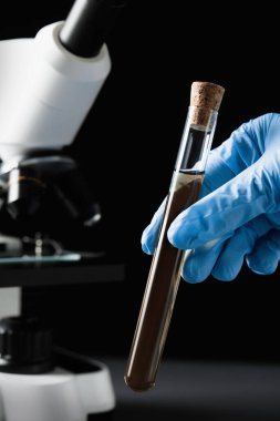 Scientist holding test tube with liquid against black background, closeup