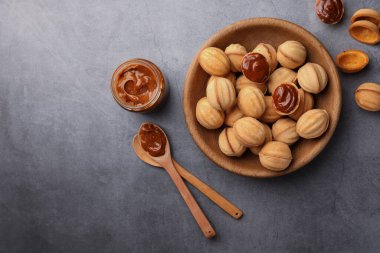 Delicious nut shaped cookies with boiled condensed milk on gray textured table, flat lay