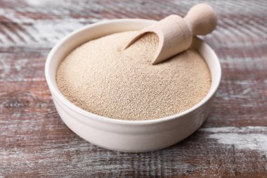 Bowl and scoop with active dry yeast on wooden table, closeup