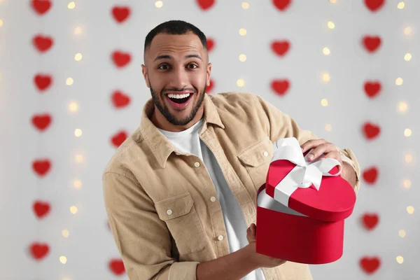 Handsome man opening gift box from his girlfriend indoors, view from camera. Valentine\'s day celebration in long distance relationship