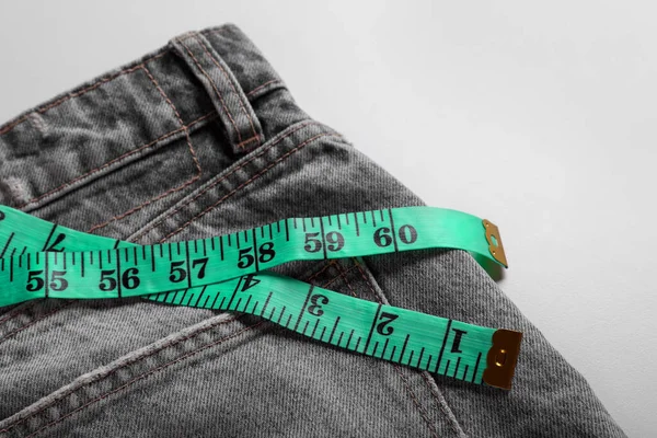 Jeans with measuring tape on light grey background, closeup. Weight loss concept