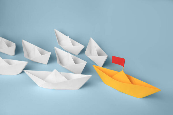 Group of paper boats following yellow one on light blue background. Leadership concept