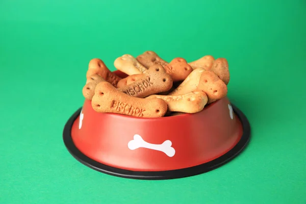 Bone shaped dog cookies in feeding bowl on green background