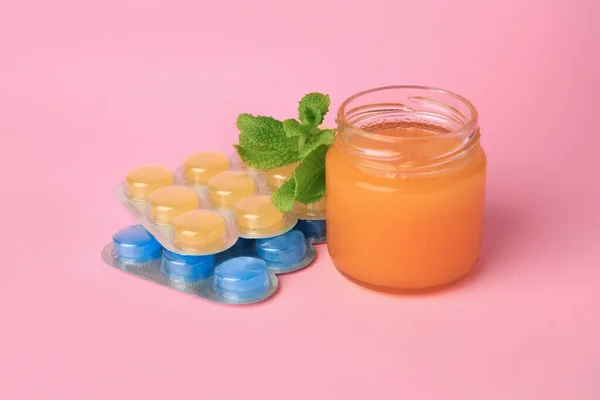 Blisters with cough drops, honey and mint on pink background