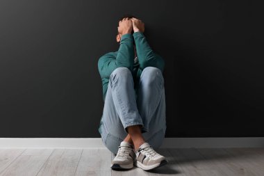 Upset man sitting on floor near black wall clipart