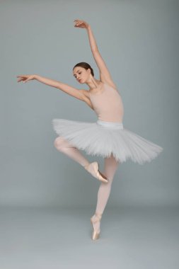 Young ballerina practicing dance moves on light grey background