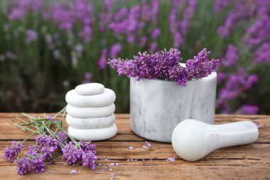 Spa taşları, taze lavanta çiçekleri ve tahta masada beyaz mermer havan topu, yakın plan.
