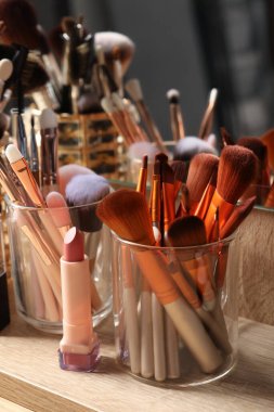 Set of professional brushes and makeup products near mirror on wooden table