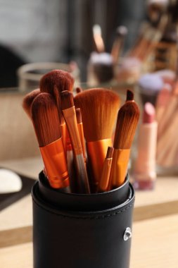 Ahşap masadaki aynanın yanında profesyonel fırçalar ve makyaj ürünleri seti, yakın plan.