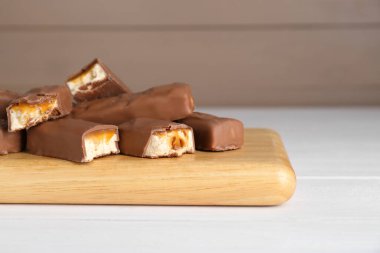 Beyaz ahşap masanın üzerinde lezzetli çikolata çubukları olan tahta, yakın plan. Metin için boşluk