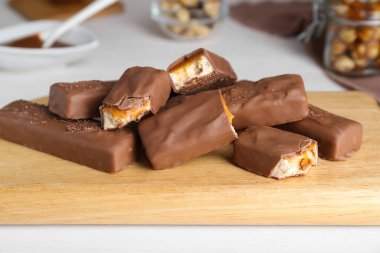 Board with delicious chocolate bars and nuts on white wooden table, closeup