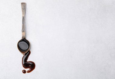 Spoon with balsamic vinegar on white table, top view. Space for text