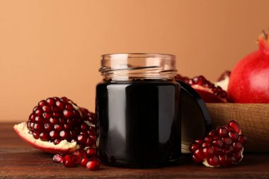 Glass jar of tasty pomegranate sauce and fresh ripe fruit on wooden table