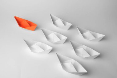 Group of paper boats following orange one on white background. Leadership concept