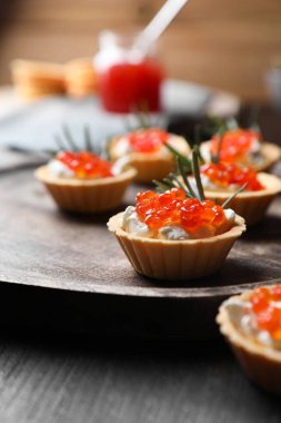 Delicious tartlets with red caviar and cream cheese served on wooden table, closeup