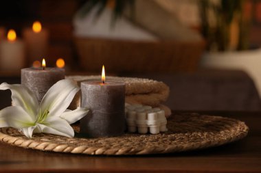 Spa composition with burning candles, lily flower and towels on wooden table in wellness center, space for text