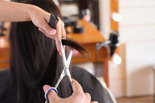 Professional hairdresser cutting woman's hair in beauty salon, closeup