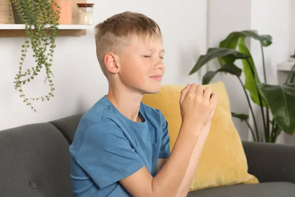 Boy with clasped hands praying on sofa at home