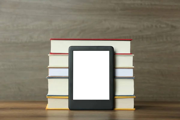 Portable e-book reader and stack of hardcover books on wooden table
