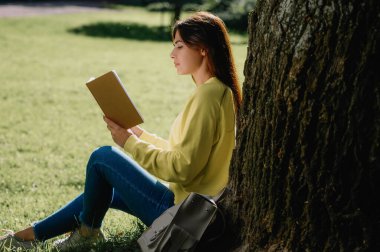 Güneşli bir günde parkta kitap okuyan genç bir kadın.
