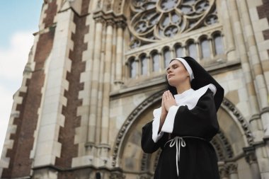 Katedralin yanında dua ederken elleri birbirine kenetlenmiş genç bir rahibe. Düşük açılı. Metin için boşluk