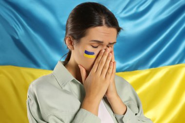 Ukrayna bayrağının yanında elleri sımsıkı bağlı üzgün genç bir kadın.