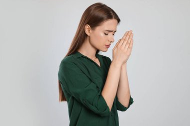 Woman with clasped hands praying on light grey background