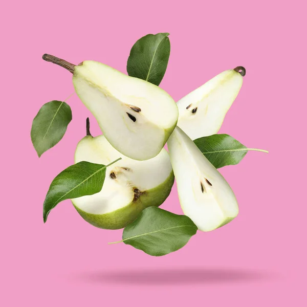 Fresh ripe cut pears and green leaves falling on pink background