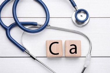Cubes with symbol Ca (Calcium) and stethoscope on white wooden table, top view