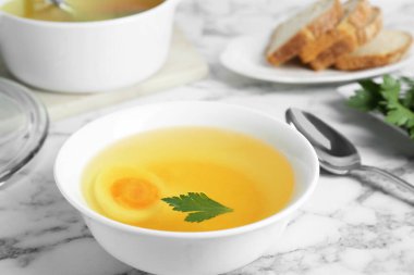 Delicious bouillon with egg and parsley in bowl on white marble table