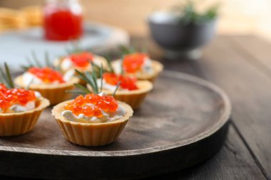 Delicious tartlets with red caviar and cream cheese served on wooden table, closeup. Space for text