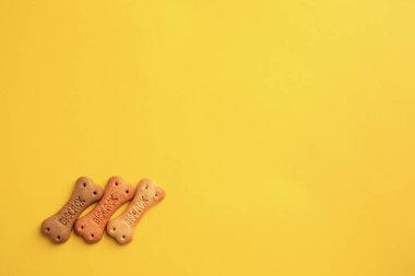 Bone shaped dog cookies on yellow background, flat lay. Space for text
