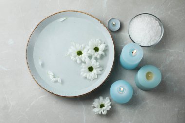 Su ve çiçeklerle dolu bir kâse, yanan mumlar, gri mermer zeminde deniz tuzu, düz bir yer. Pedikür prosedürü