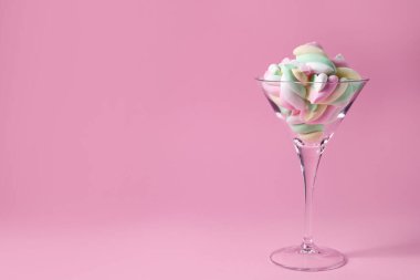 Pembe arka planda renkli marşmelovlarla güzel bir martini bardağı. Metin için boşluk