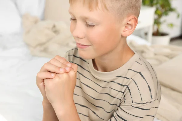 Boy with clasped hands praying at home, closeup