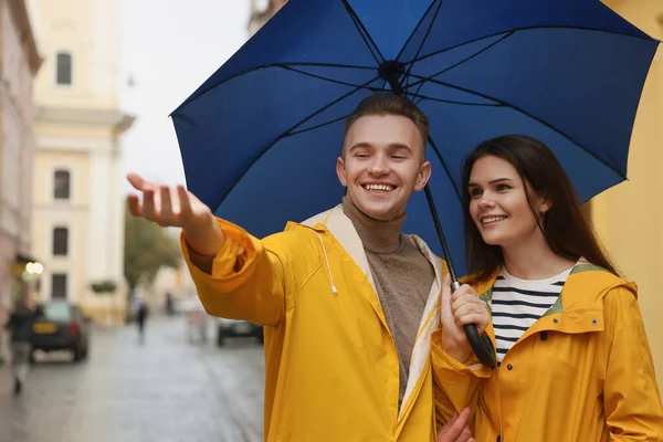 Lovely young couple with umbrella walking under rain on city street