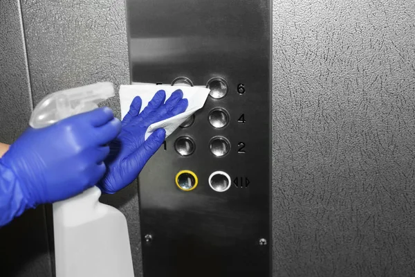 Woman wiping buttons of elevator`s panel with detergent and paper napkin, closeup