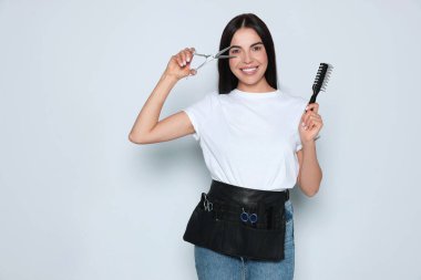 Portrait of happy hairdresser with professional scissors and vent brush on light background