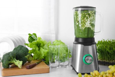 Blender with delicious smoothie and ingredients in kitchen