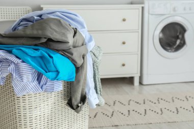 Plastic laundry basket overfilled with clothes in bathroom, closeup. Space for text