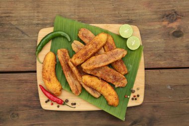 Lezzetli kızarmış muzlar, farklı biberler ve ahşap masa üzerinde limon dilimleri.