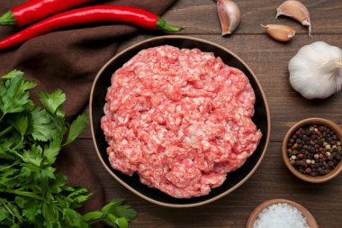 Bowl of raw fresh minced meat and ingredients on wooden table, flat lay