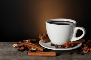 Cup of delicious hot chocolate, spices and coffee beans on wooden table. Space for text